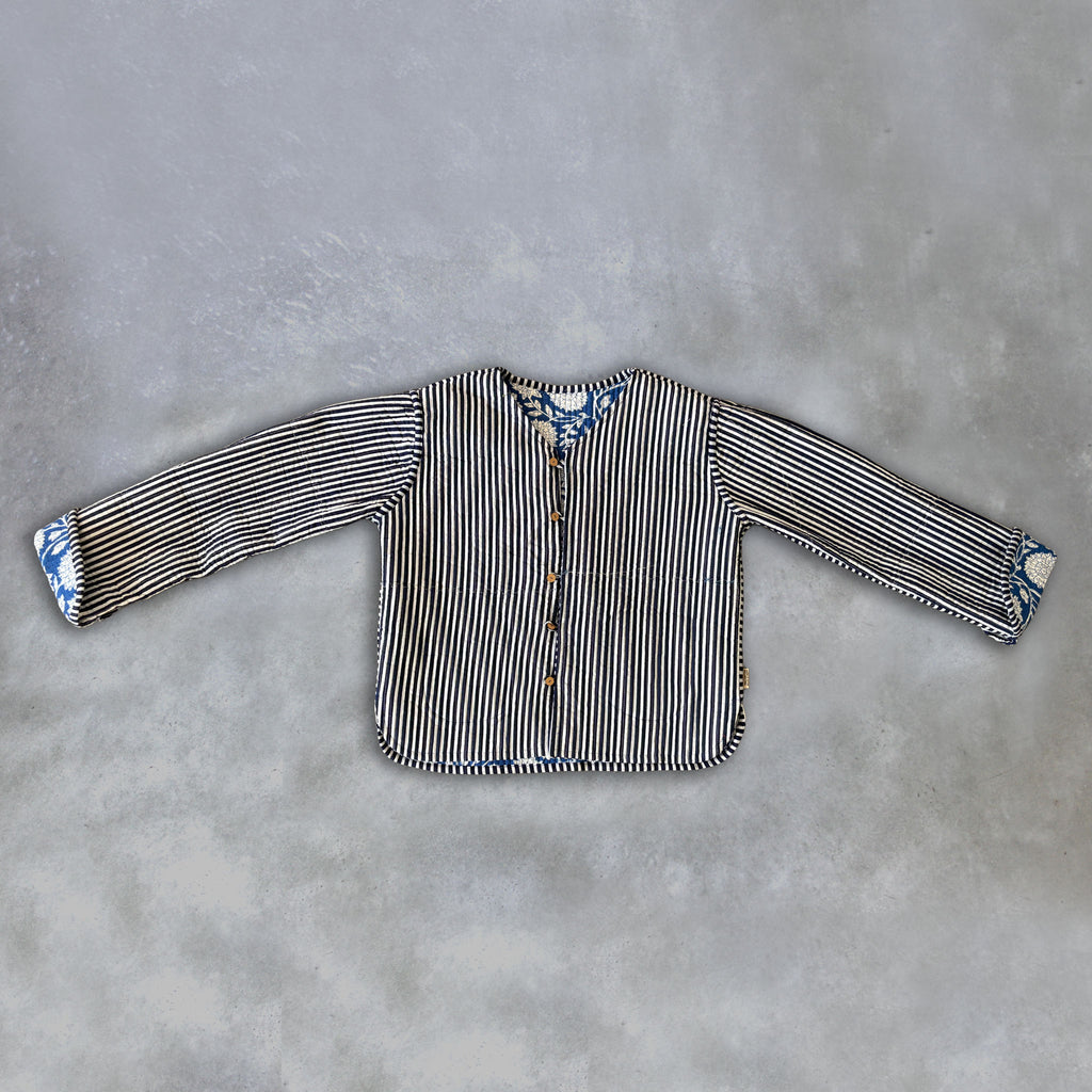 A long-sleeve inside of a Colourstory blue jacket striped with black and white vertical stripes and blue floral-patterned cuffs, laid flat on a textured grey background.