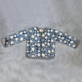 A long-sleeve quilted jacket by Colourstory featuring a blue and white floral block print with striped black and white trim, laid flat on a textured gray background.