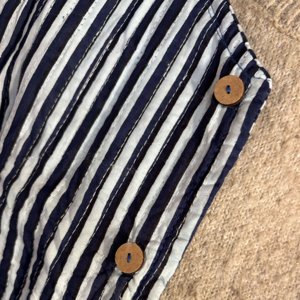 Close-up of a navy blue and white striped jacket by Colourstory with two round wooden buttons, laid on a beige textured surface.