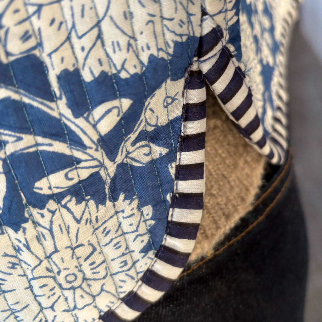 Close-up of a Colourstory quilted jacket with a blue and cream floral block-print pattern, striped trim, and a tan fabric lining.