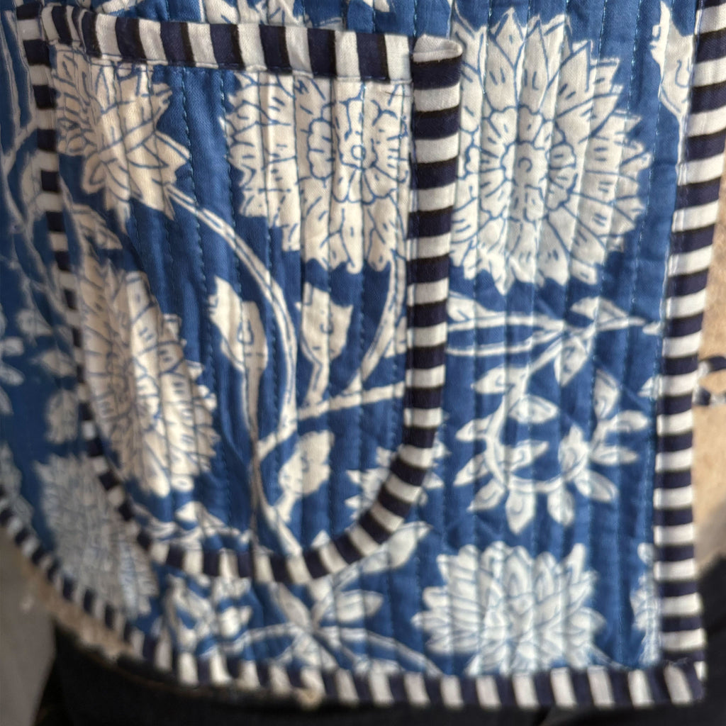 A close-up of a quilted Colourstory jacket,  featuring a blue and white floral block-print style pattern with dark navy and white striped piping on the pocket.