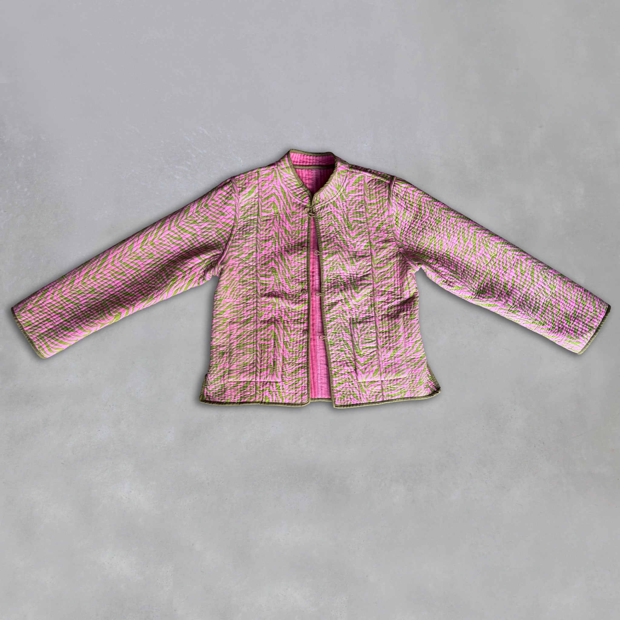 A pink quilted Colourstory jacket with a textured, zebra-like pattern in pink, green, and olive green trim laid flat on a grey background.