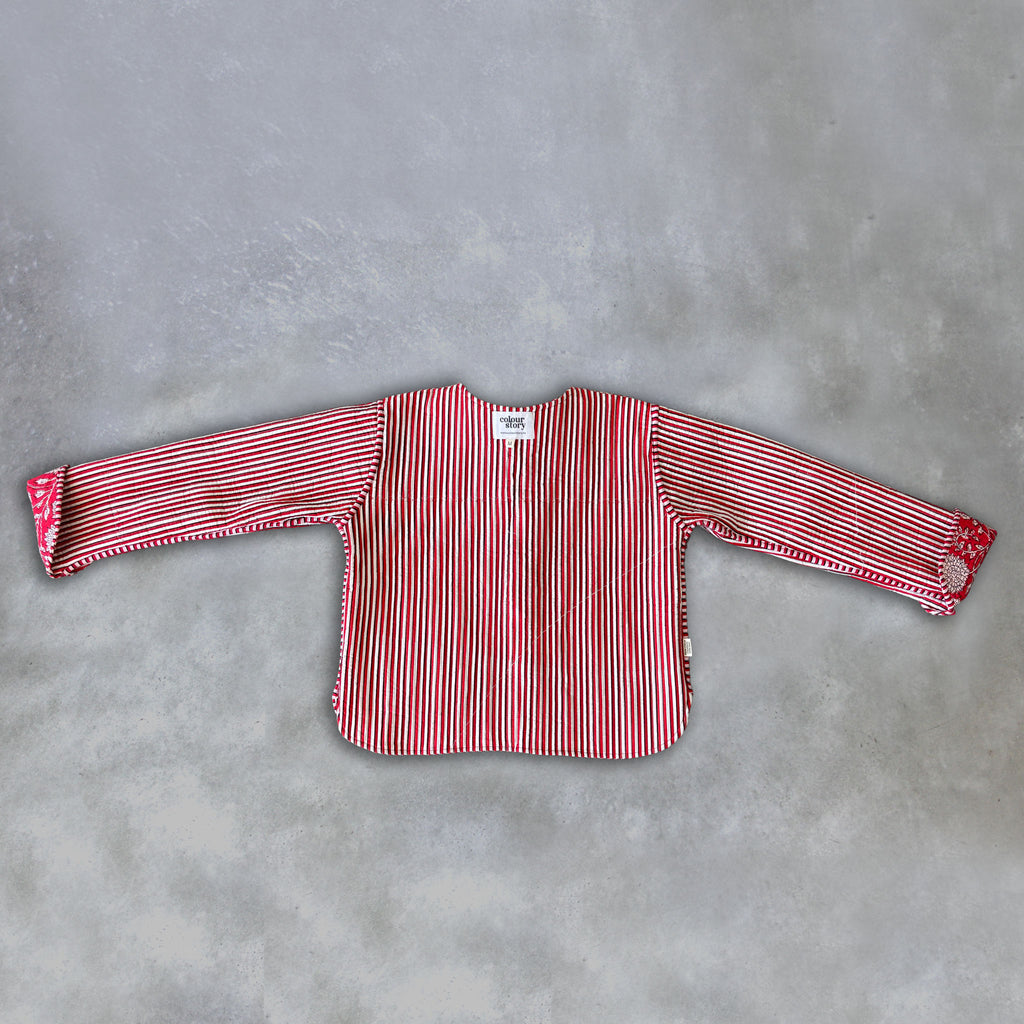 Inside of a Colourstory red jacket with red and white, black vertical stripes, laid flat on a textured grey background.