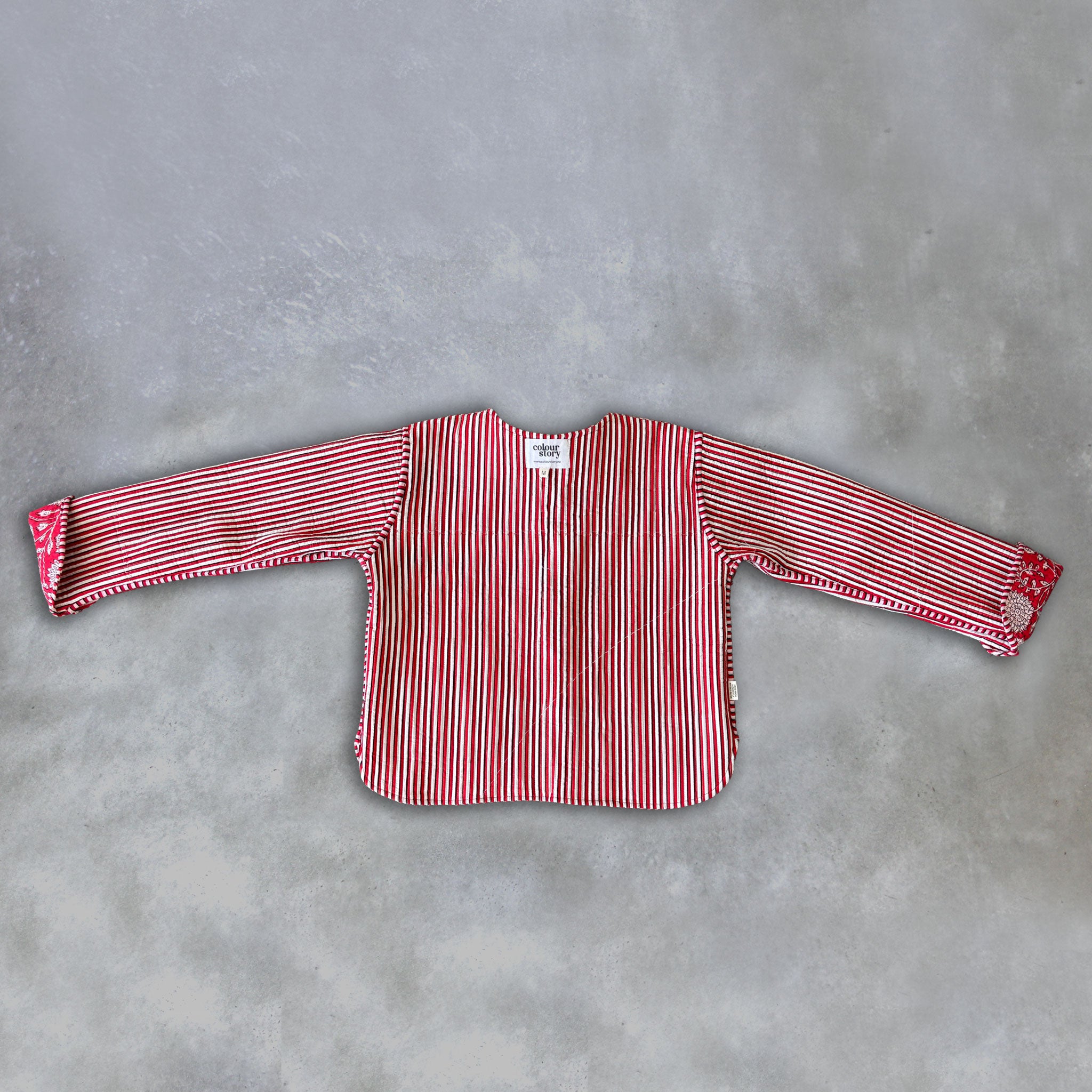 Inside of a Colourstory red jacket with red and white, black vertical stripes, laid flat on a textured grey background.