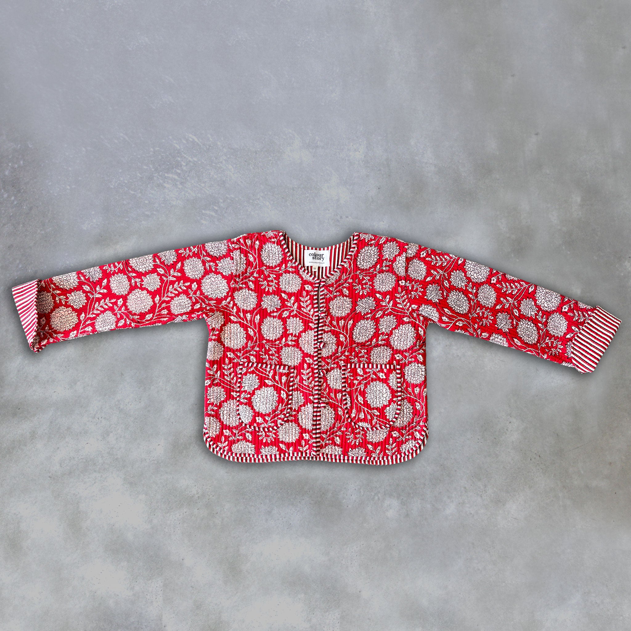 A red long-sleeve jacket by Colourstory with a white floral and circular pattern, laid flat on a textured grey background.