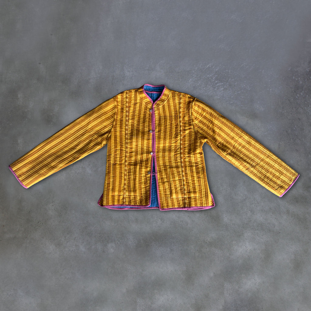 A Colourstory yellow and mustard striped jacket with pink trim, laid flat on a textured grey background.