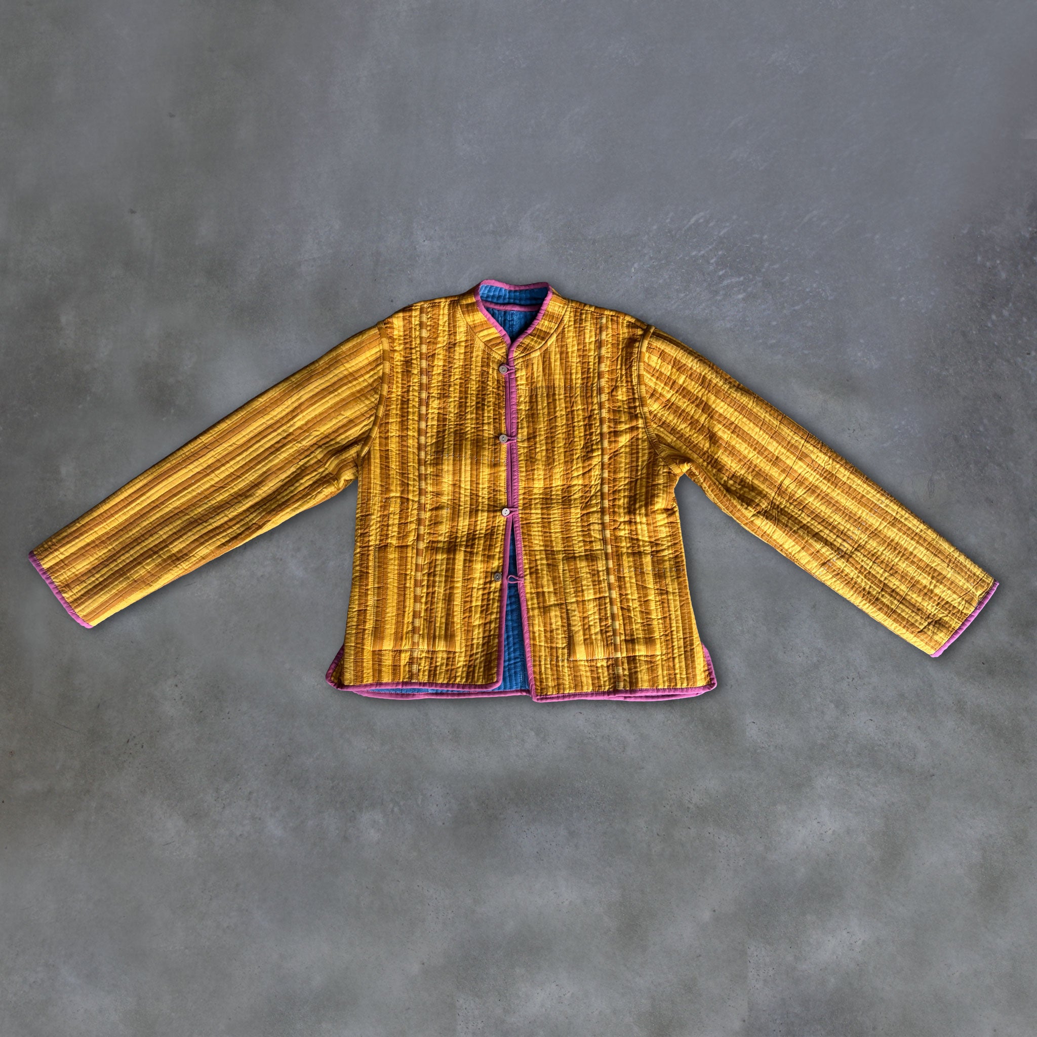 A Colourstory yellow and mustard striped jacket with pink trim, laid flat on a textured grey background.