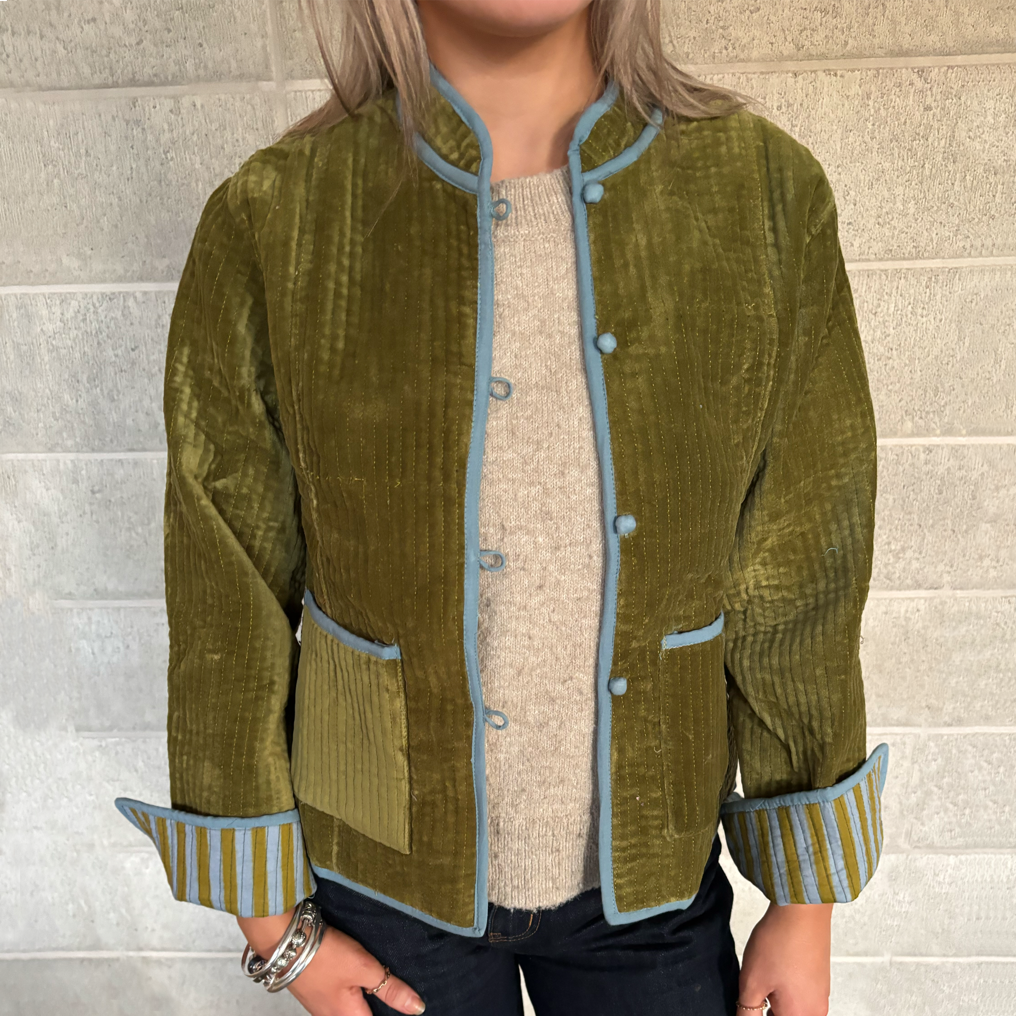 ColourStory model wearing a olive green velvet jacket with light blue trim, striped cuffs.