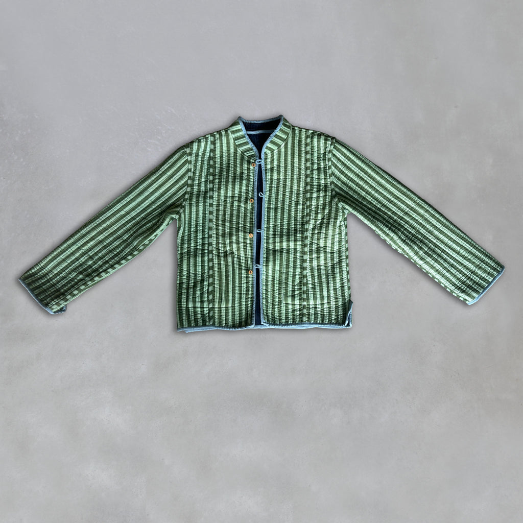 A green and sage green vertically striped quilted jacket with a mandarin collar and front button closure, laid flat on a textured grey background.