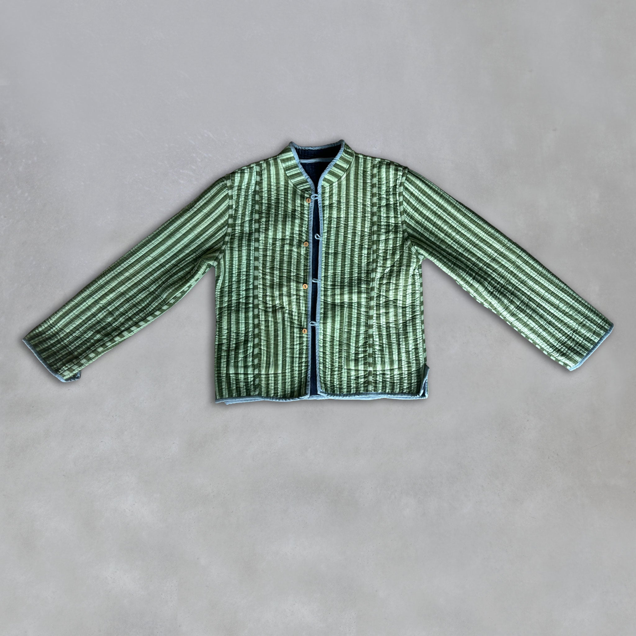 A green and sage green vertically striped quilted jacket with a mandarin collar and front button closure, laid flat on a textured grey background.