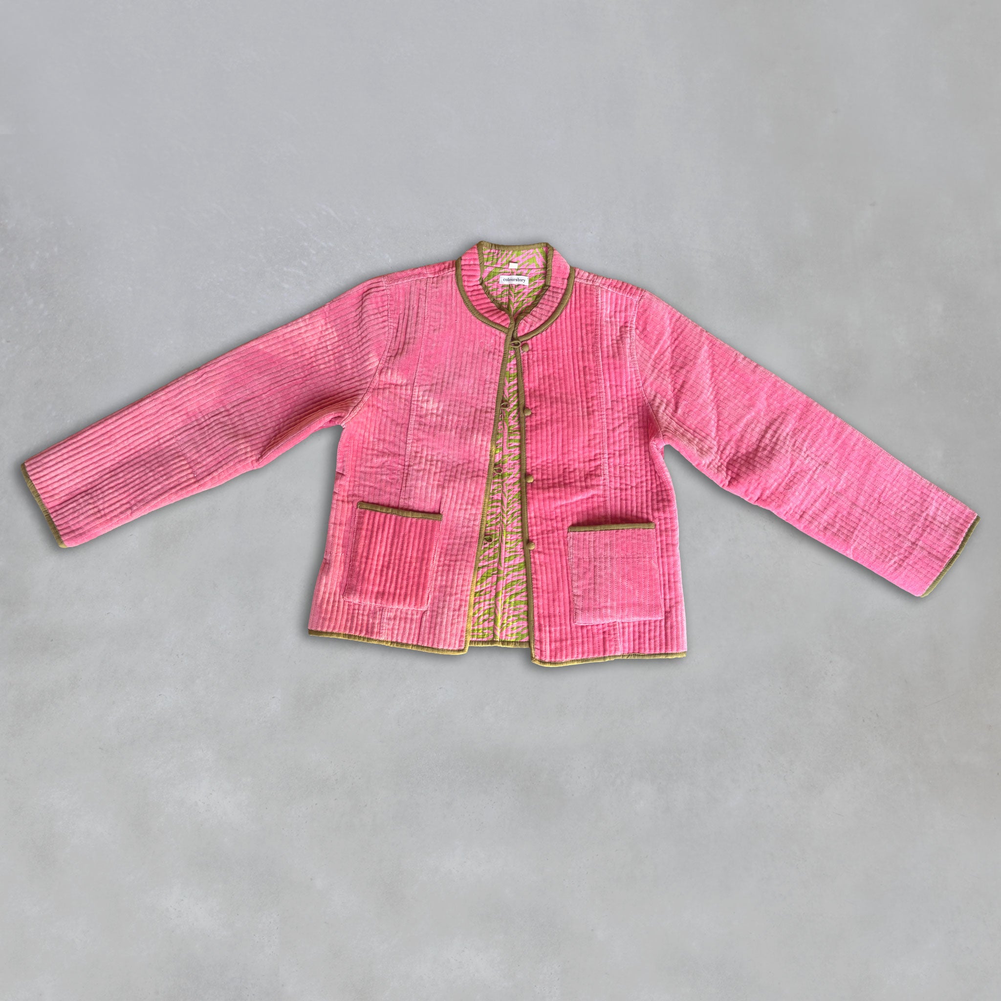 A Colourstory pink velvet jacket with olive green trim and button closures, laid flat on a grey background.