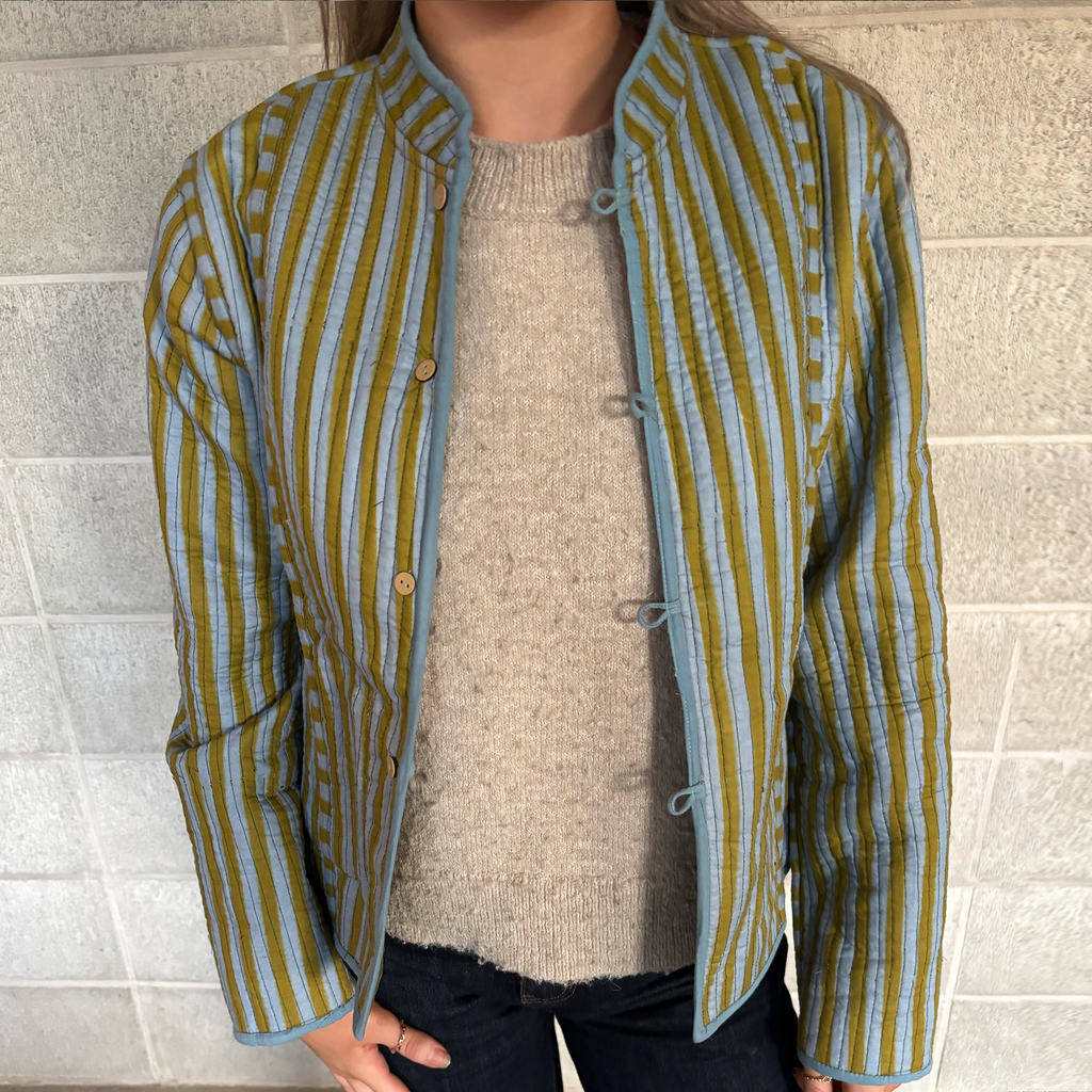 Our ColourStory model is wearing a cropped, long-sleeve quilted jacket with vertical olive green and light blue stripes, featuring a mandarin collar and button-tab closure, layered over a beige knit sweater.
