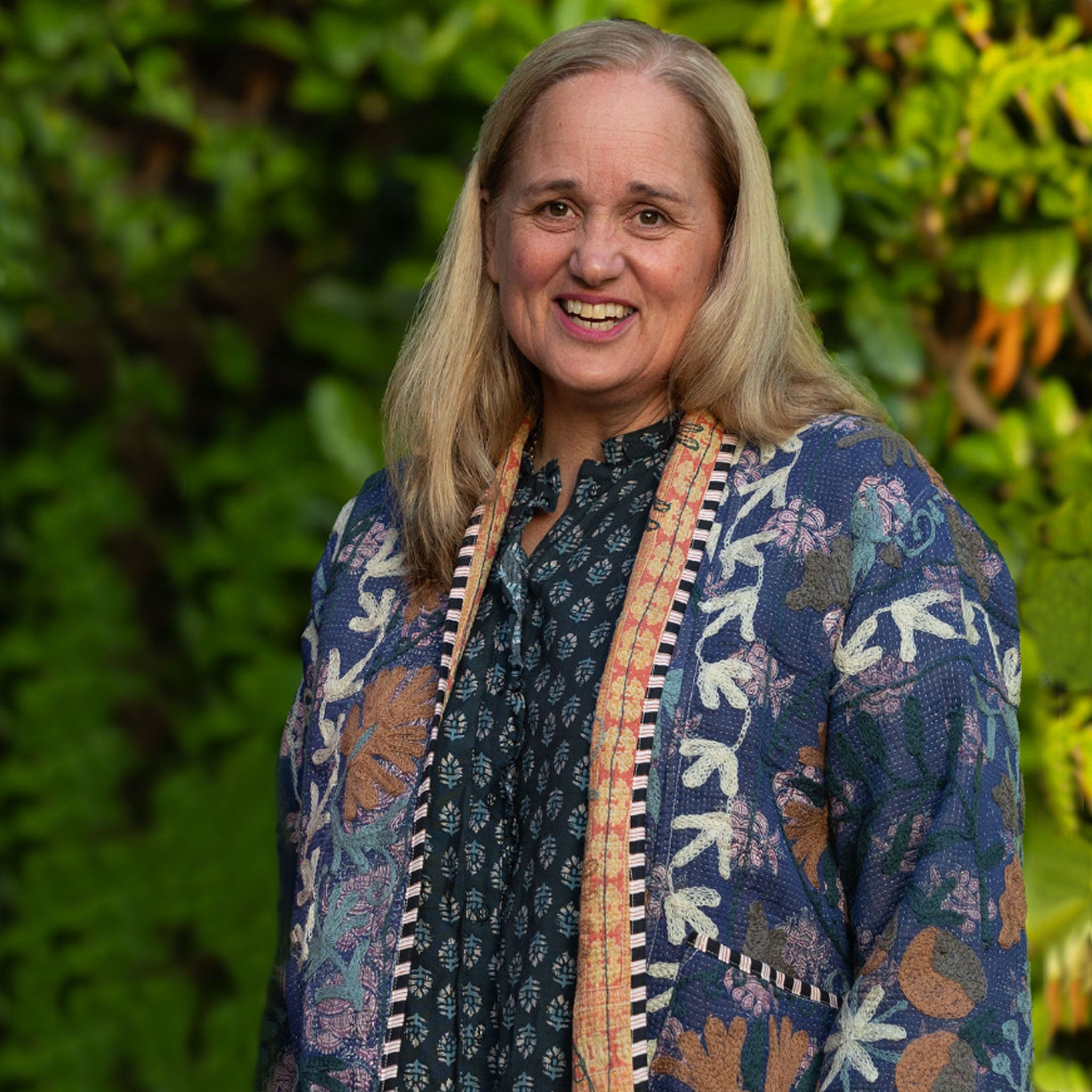 Woman (Lucy) wearing a Kantha jacket in front of green foliage