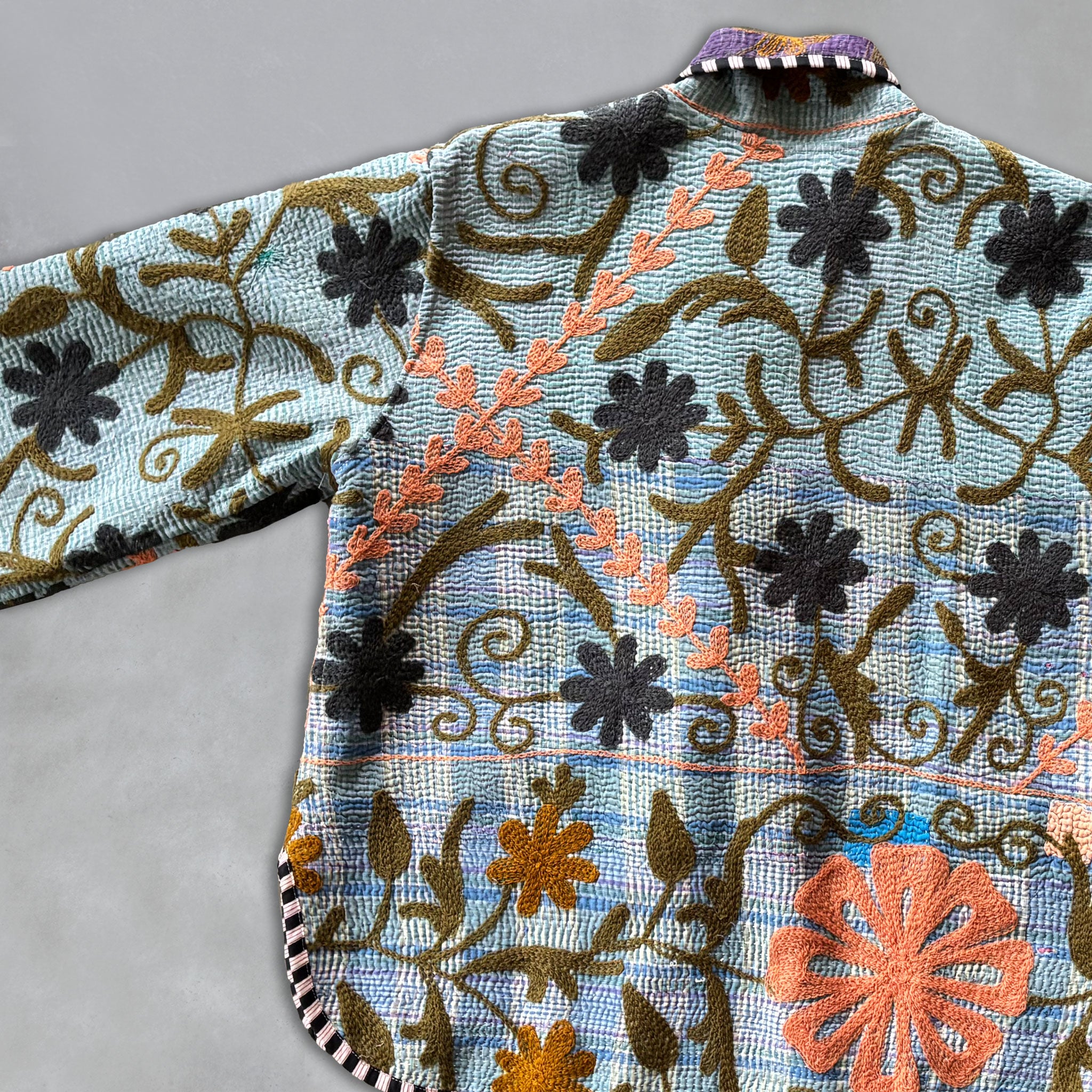 Embroidered fabric with floral patterns on a Kantha Jacket on a grey background