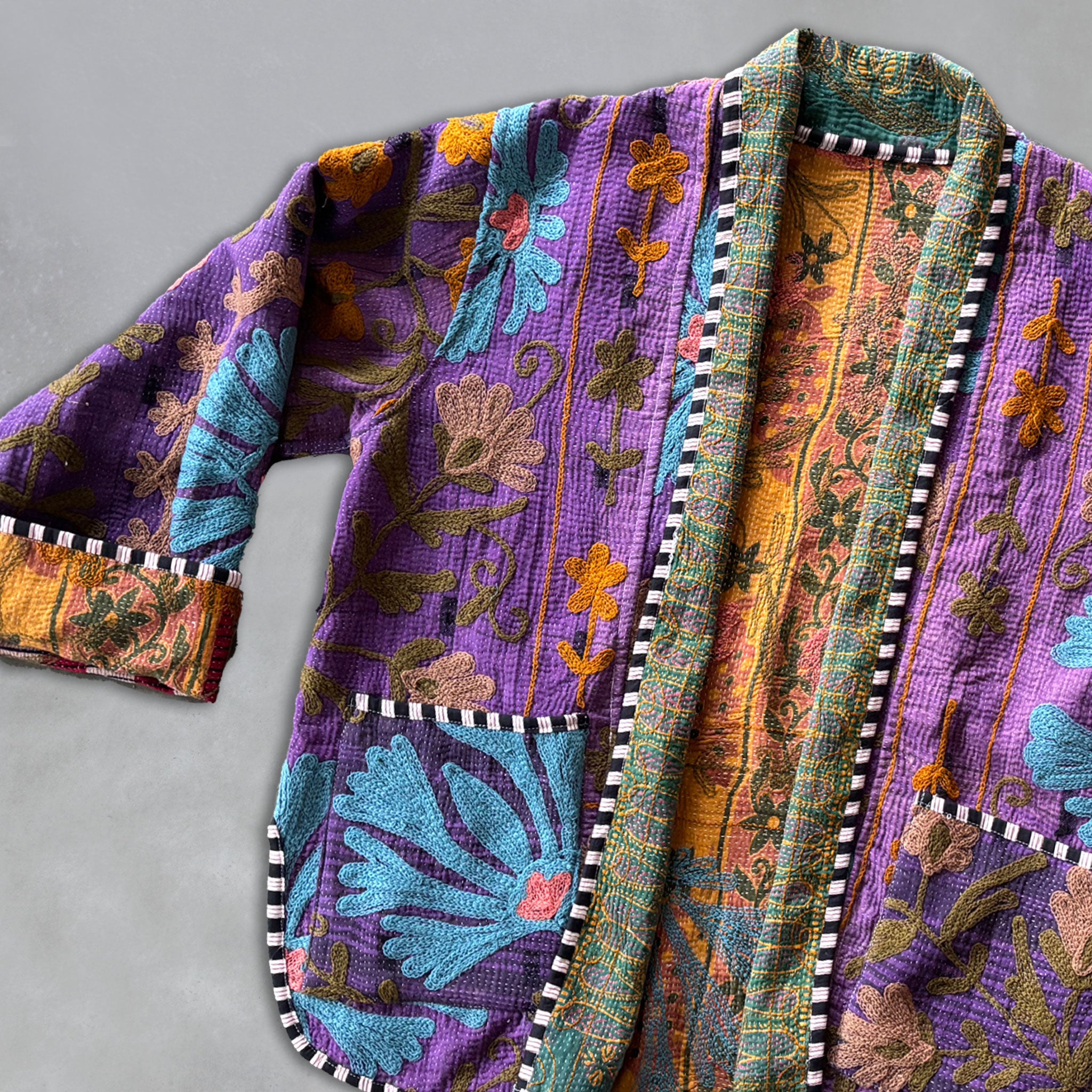 Colourful, floral-patterned Kantha fabric on a purple jacket with a grey background by Colourstory.