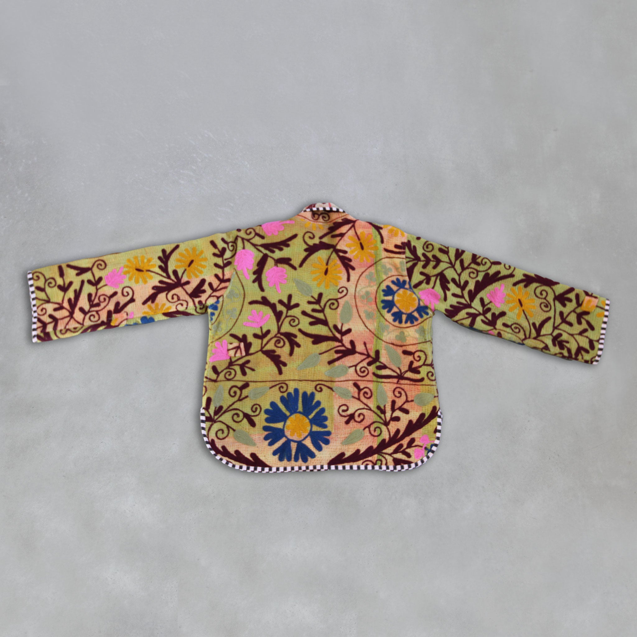Colourful embroidered Kantha jacket on a grey background.