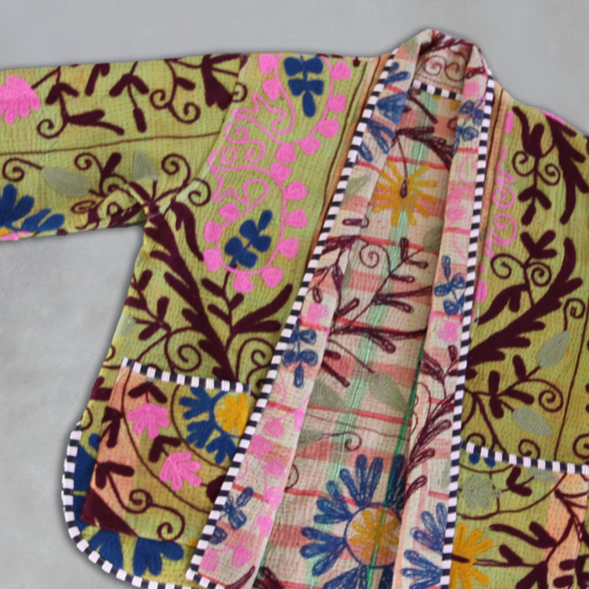 Colourful fabric Kantha jacket by Colourstory with intricate patterns on a grey background.